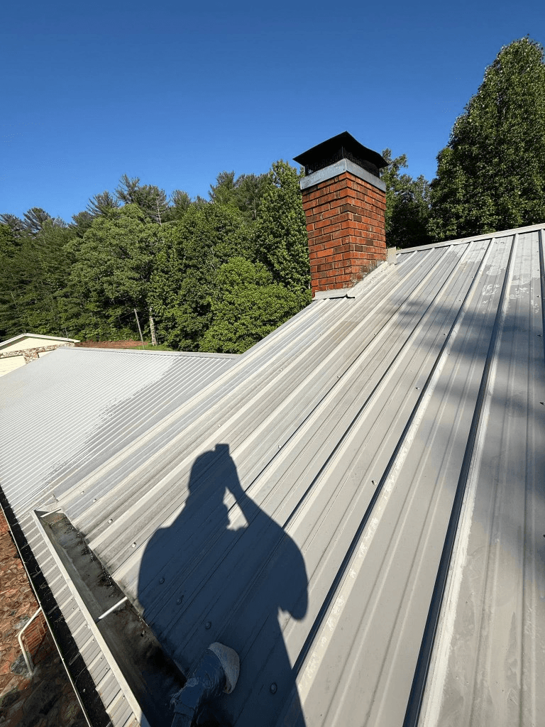 Clean corrugated metal roof with brick chimney under a blue sky